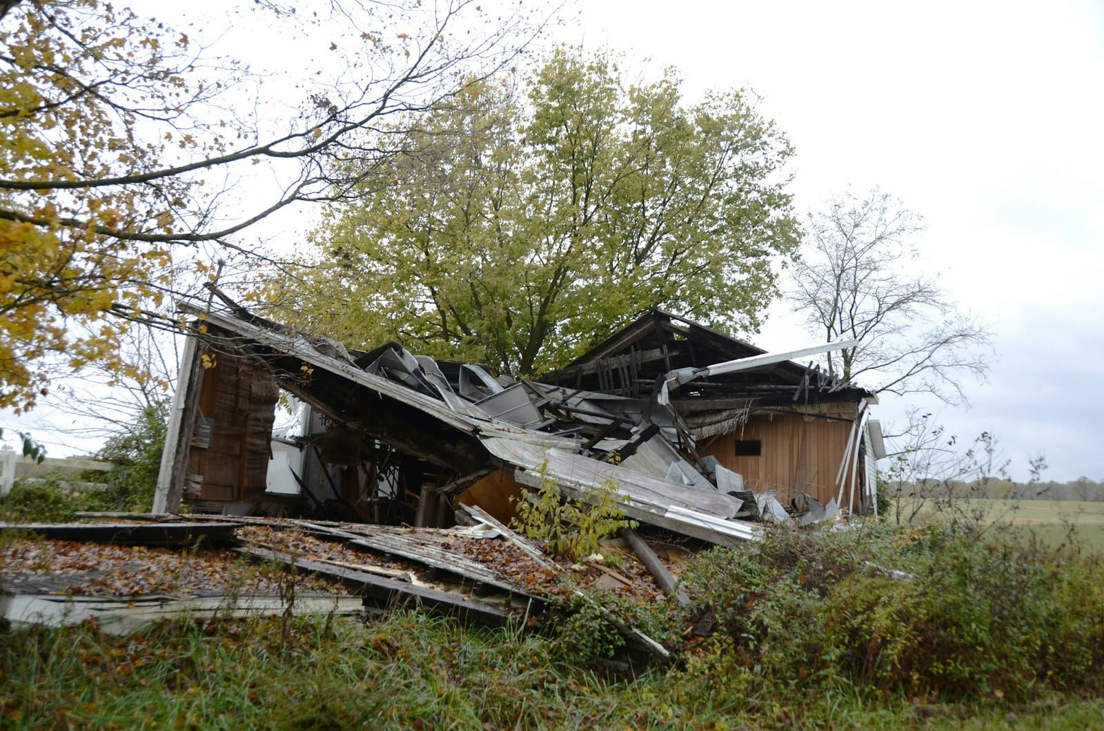 A dilapidated wooden house collapsing in a field.